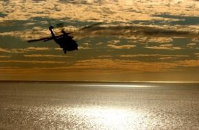 helicopter in sunset sky above calm water