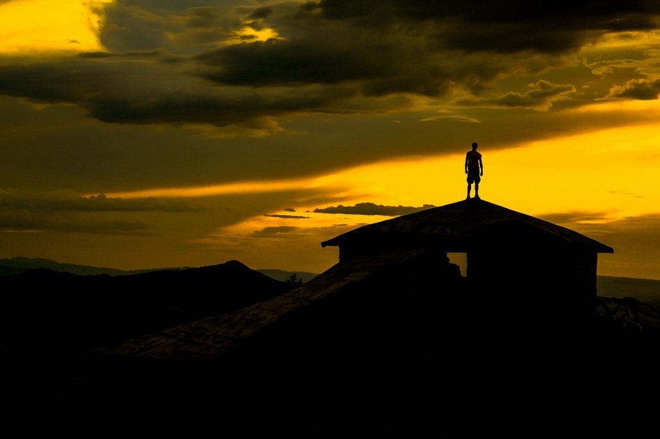 silhouette of a man on the roof of a building during sunset