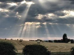 scenery sun rays from cloudy sky above harvested field
