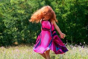 red-haired girl in a purple dress is dancing in a meadow