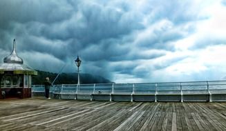 man fishing on wooden pier under dramatic clouds