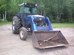 Blue tractor with bucket among the plants