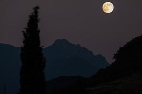 white moon in the night sky over the mountains