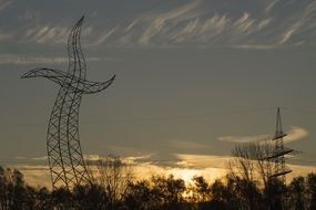 high voltage power line at evening sky with beautiful and colorful light behind the tree
