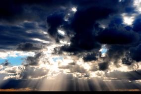 bright sunbeams through dark blue clouds in the evening sky