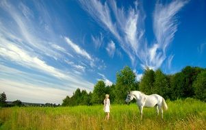 girl with a white horse among green meadow