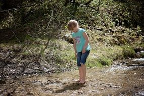 girl stands barefoot in a forest stream