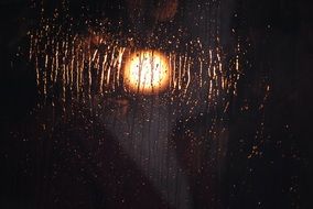 light in darkness through glass with rain drops