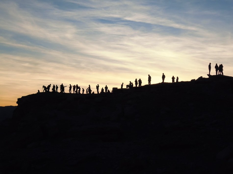 people silhouettes on rock at sunset sky