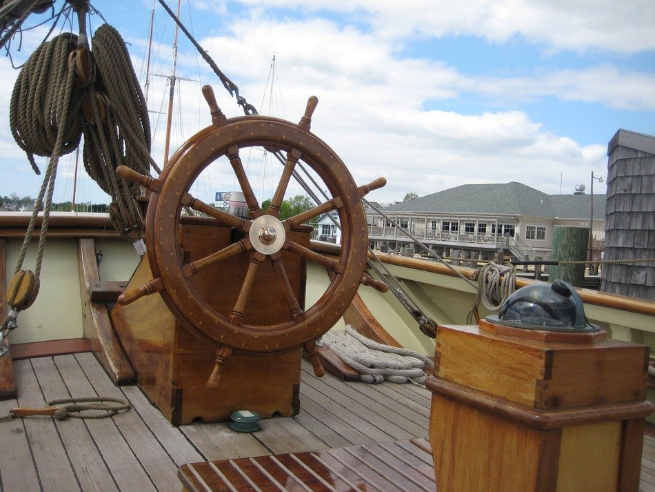 Wooden wheel on the deck at blue sky background with white clouds