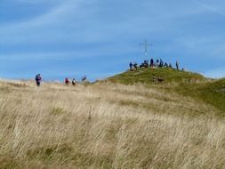 people near the cross on a hill in the alps