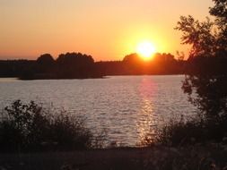 sunset on lake with trees silhouettes