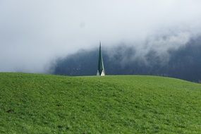 spire behind a green hill