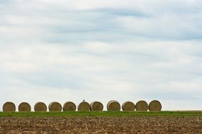 even row of straw bales on the green field at blue sky background with white clouds