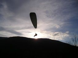 paraglider silhouette in sky above hill