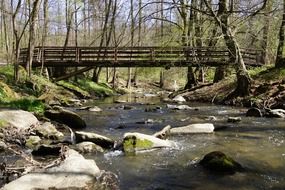 wooden bridge across river with stones on bed in forest at spring