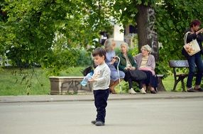 Boy with bottle in the beautiful park with people on the benches and green plants