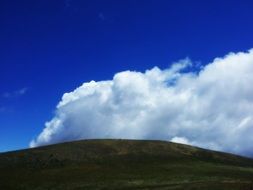 fluffy clouds over green hill