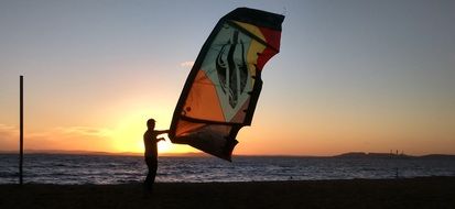 man with paraglider wing in front of sea at sunset