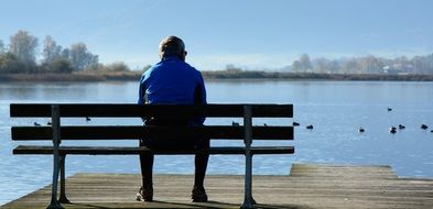 person sits on bench in front of water