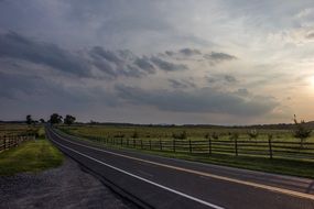 landscape of paved road along pasture at the sunset