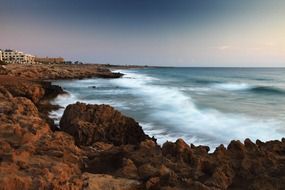 blurred waves at red rock coast, evening seascape