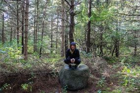 A girl sits on a stone near a tree in the forest
