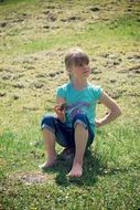 little girl sitting among green meadow