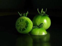 cut green tomatoes on black background