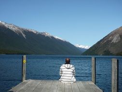 man sitting on pier at mountain lake, new zealand