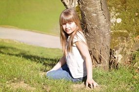 little girl with blond hair near a tree on a sunny day