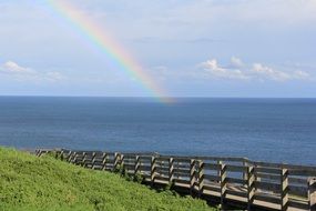 photo of a wooden bridge and a rainbow over the sea