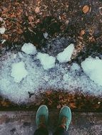 feet in green sneakers on ground near snow