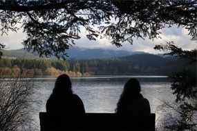 silhouettes of people sitting on a bench by the pond