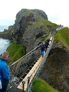 people walking on long winding rope bridge on rocks at sea