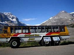 Colorful tourist bus near the beautiful rocky mountains in snow at blue sky on Athabasca Glacier in Canada