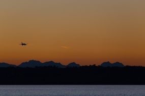 A plane flies over the lake during sunset