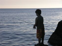 a little boy is fishing on the shore