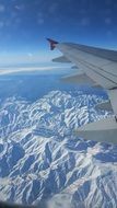 part of airplane wing above snowy mountains