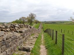 fenced pathway along ruined stone wall