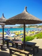 Beach tables with benches under straw umbrellas on the beautiful beach at blue sky background