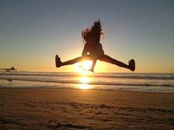 child girl jumping at colorful sunset background on the beach