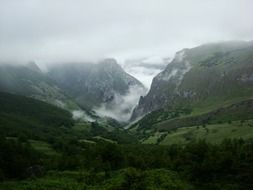 clouds above picturesque green mountain valley, spain, asturia, peak urriellu