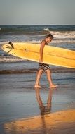 young man with a brown surfboard in his hands on the evening beach
