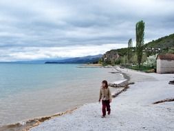 little girl walks by the sea in cold time