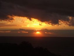 landscape of black water and black clouds in the middle of the fiery sun