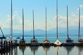 row of sailing boats at pier in view of blue mountains