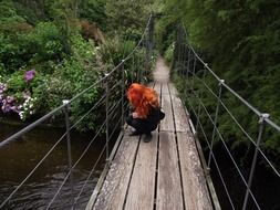 red-haired girl on a wooden suspension bridge