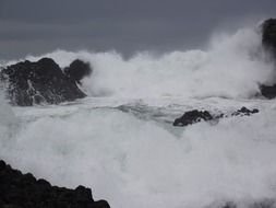 Beautiful white ocean waves are beating against the rocks at cloudy sky background