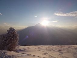sun behind the mountains in the background of a snowy landscape